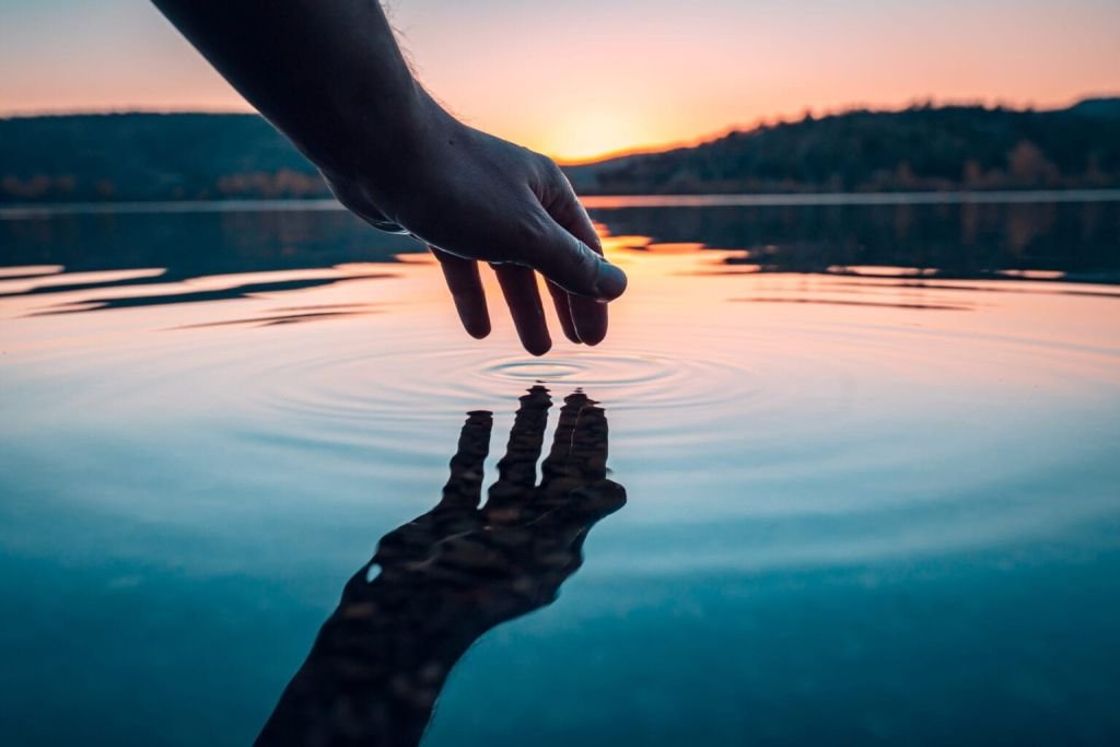 hand-touching-water-surface-at-sunset